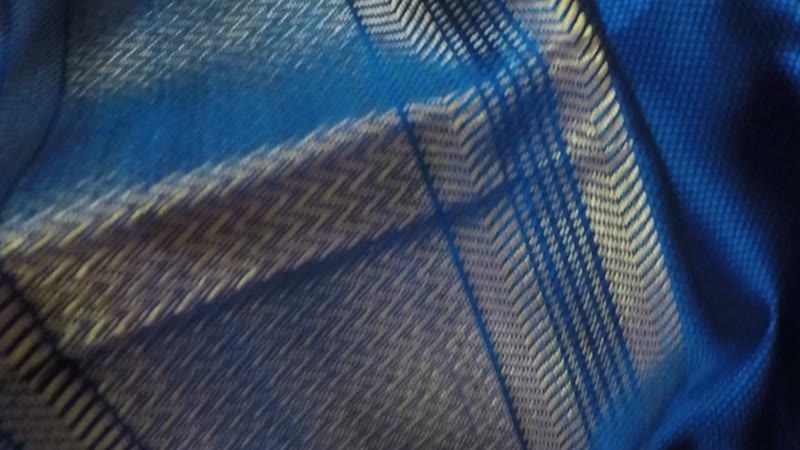Close view of blue cloth with a woven gold and dark border