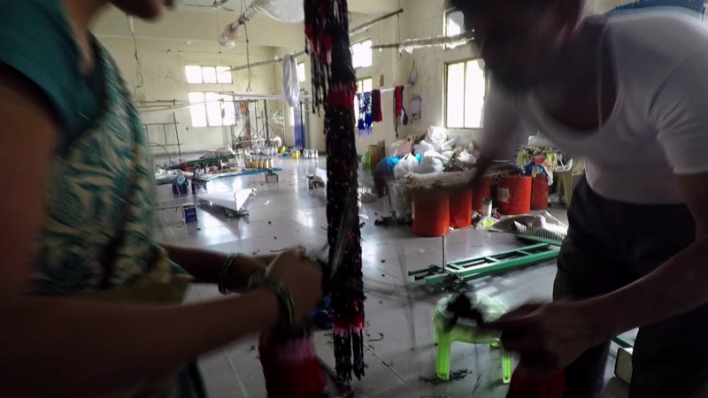 Two artisans lifting a long bundle of tied and dyed yarn in a workshop